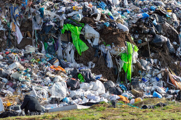 Workers sift through a large mound of plastic waste in a landfill, highlighting the impact of pollution on the environment