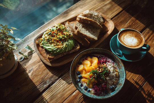 top-down view of a healthy breakfast on a wooden table, avocado toast, smoothie bowl, cup of coffee, bright natural light, minimal food styling