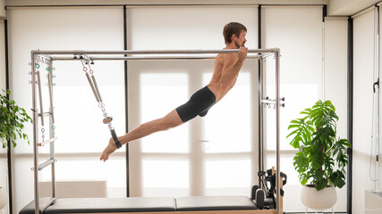 A man performs aerial exercises on a reformer machine.