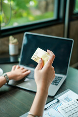 A person holding a credit card while using a laptop, symbolizing online shopping and digital transactions.