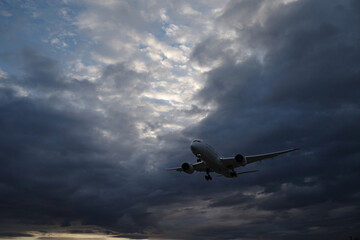曇り空の早朝、着陸態勢で上空を飛んでいく飛行機