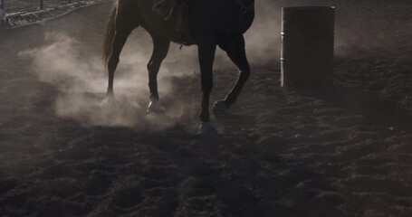 Cinematic, silhouette low shot of horse and rider kicking up dust as they run around ring - slow motion