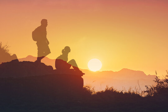 silhouette of a man and woman on a mountain looking out to the sunset  - Powered by Adobe