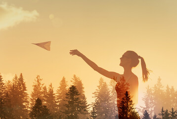 Woman throwing paper airplane and launch on the background of bright sun  treetops and picturesque sunset, freedom, vision, future concept 