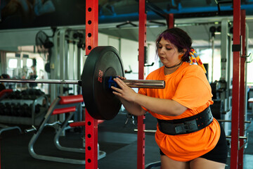 View of an overweight young Latina woman carrying weights and preparing to workout at a gym. Pushing herself. Improvement and well-being.