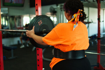 View of an overweight young Latina woman carrying weights and preparing to workout at a gym. Pushing herself. Improvement and well-being.