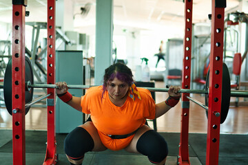 View of a beautiful, overweight young Latina lifting weights and working out at a gym. Positively, she's pushing herself to the limit. She's improving and feeling better.