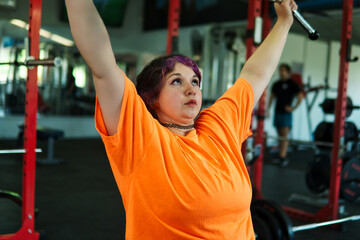 Beautiful, overweight Latina woman concentrating on lifting weights on an exercise machine at a gym. Wearing colorful clothes, hair, and retro makeup, she's positive. She's pushing herself.