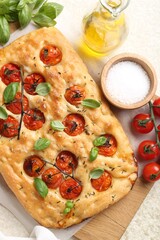 Delicious focaccia with tomatoes, spices and oil on beige table, flat lay