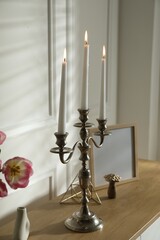 Elegant candlestick with burning candles and decor on table near white wall