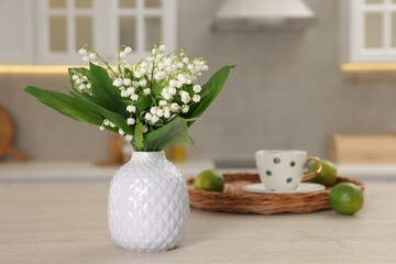 Beautiful lily-of-the-valley in vase, limes and cup of tea on wooden table in kitchen, closeup