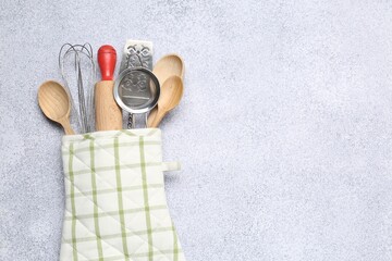Different kitchen utensils in oven mitten on light table, top view. Space for text