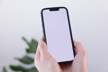 Woman holding smartphone with blank screen on blurred background, closeup. Mockup for design