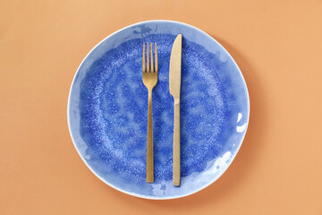 Empty plate and cutlery on light orange background, top view