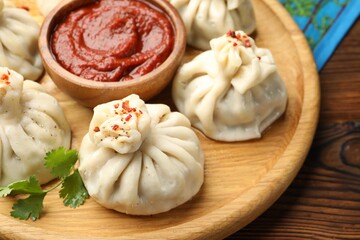 Delicious khinkali served with sauce on wooden table, closeup