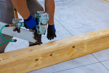 Craftsman focuses on nailing wooden beams together at construction site using pneumatic nail gun