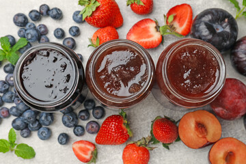 Different sweet jams in jars and ingredients on grey table, flat lay