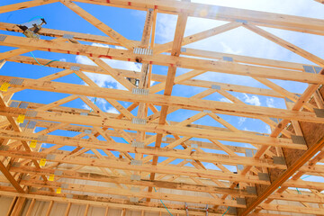 Workers are constructing wooden roof trusses frame with exposed beams under bright blue sky.