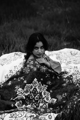 Girl wrapped in a luxurious silk carpet, seated on an intricately embroidered sheet laid over...
