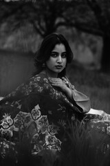 Girl wrapped in a luxurious silk carpet, seated on an intricately embroidered sheet laid over...