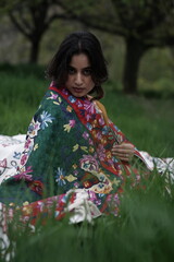 Girl wrapped in a luxurious silk carpet, seated on an intricately embroidered sheet laid over...
