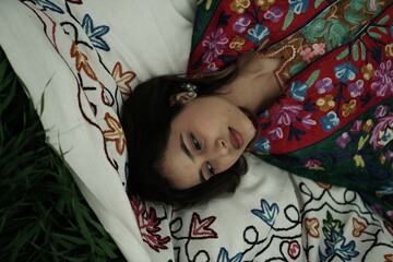 Woman lying peacefully on a traditional carpet spread over lush green grass, blending comfort,...