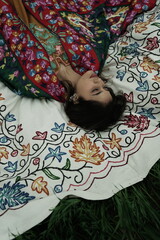 Woman lying peacefully on a traditional carpet spread over lush green grass, blending comfort,...