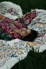 Woman lying peacefully on a traditional carpet spread over lush green grass, blending comfort,...