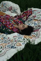 Woman lying peacefully on a traditional carpet spread over lush green grass, blending comfort,...