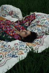 Woman lying peacefully on a traditional carpet spread over lush green grass, blending comfort,...