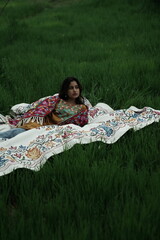 Woman lying peacefully on a traditional carpet spread over lush green grass, blending comfort,...