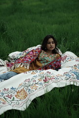 Woman lying peacefully on a traditional carpet spread over lush green grass, blending comfort,...
