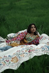 Woman lying peacefully on a traditional carpet spread over lush green grass, blending comfort,...