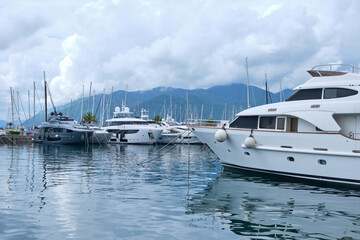 Luxury yachts docked at marina in Porto Montenegro with mountains and cloudy sky in the background