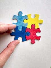 Obraz premium Hand placing colorful puzzle pieces symbolizing Autism Awareness on a white background