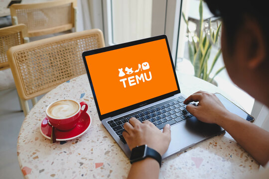 Bangkok, Thailand. June 11, 2025; Person using laptop displaying TEMU shopping app logo at terrazzo table with cappuccino cup and natural light background.