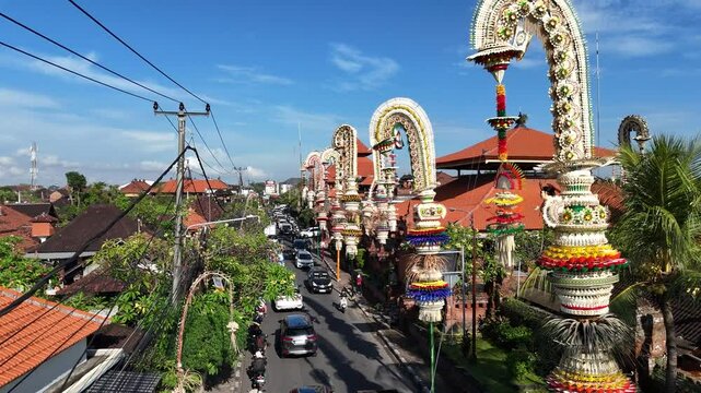  Drone aerial footage of Penjor lined up in front of a roadside temple with various decorations made of coconut leaves dyed in full color, indicating a religious
