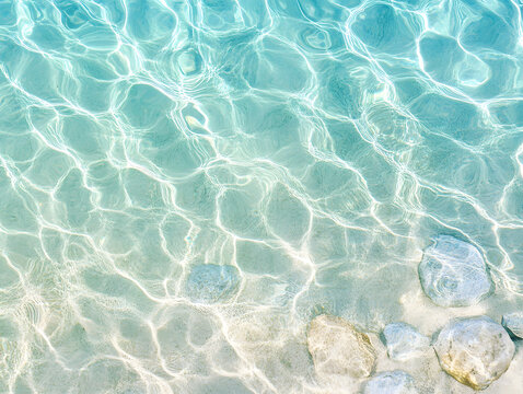 Clear water surface with sunlight reflections and smooth stones beneath, creating calm and refreshing ocean shimmer pattern in soft blue and sandy tones - Powered by Adobe