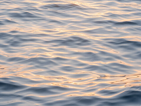 Gentle ocean water surface with soft golden light reflections creating calm and peaceful atmosphere in early morning or late afternoon - Powered by Adobe