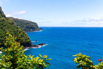 Lush green cliffs meet the deep blue sea under a clear sky in Maui, Hawaii.
