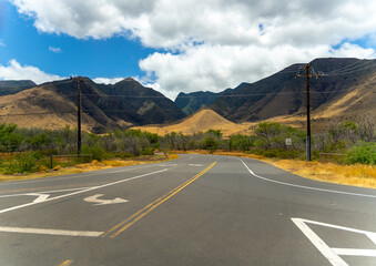 Road curves through a valley with mountains under a blue sky with white clouds.