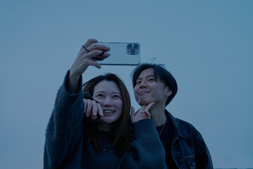 夕闇が迫る海岸で写真を撮る若い男女