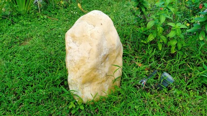 A pale yellow garden stone placed on a green grassy lawn, adding a natural decorative element to...
