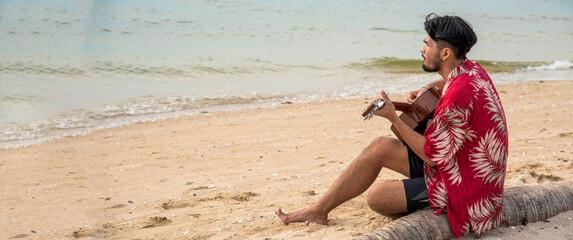 Banner Young men playing acoustic guitar on the beach. Happy man person playing acoustic guitar music instrument seaside sitting on sand tropical beach island. Happy guitarist hobby with copy space