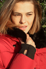Headshot of beautiful young woman in red winter jacket with black details by natural  
 warm sunset colour sunlight. Fashion model with natural make up and hair in puffer jacket
