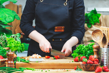 Chef cooking food in the kitchen. Cook cuts yummy strawberries, prepare gourmet salad. Wooden...