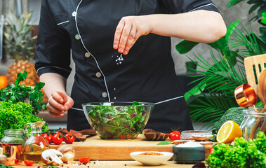 Cooking food in the kitchen. Chef sprinkle salad with chili flakes, wooden table with kitchenware, vegetables, herbs and ingredients. Healthy vega eating, recipes, blogging