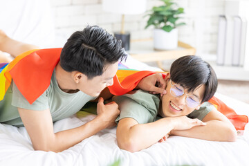 Obraz premium Portrait of carefree gay couple with lgbt flag on the bed, Gay couple love, happy together concept. LGBTQI lifestyles at home.