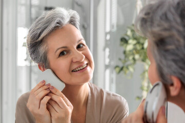 Elderly woman pensioner with gray hair middle-aged does facial massage with microcurrent massager