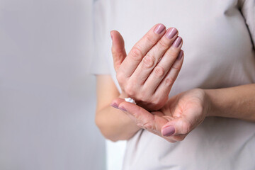 A mature woman of the pensioner age with dry skin smears moisturizing cream on her hands.